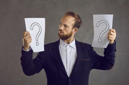 Businessman looking between two question mark sheets