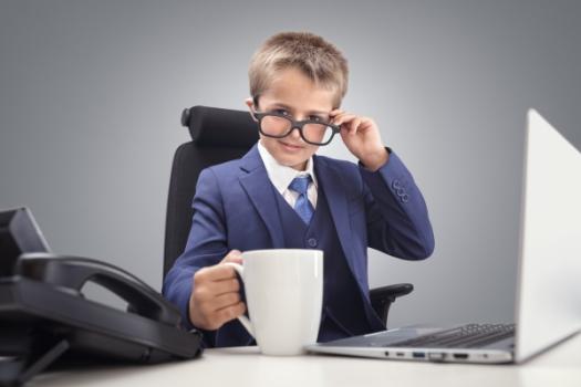 A boy in suit at desk with coffee laptop