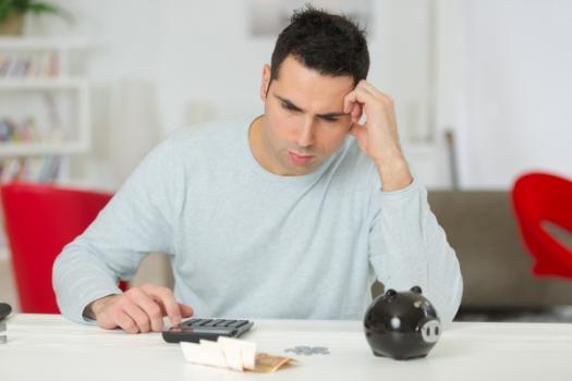 Man worried next to piggy bank calculator